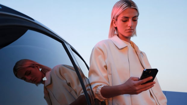 Een vrouw checkt haar smartphone naast een Peugeot E-308