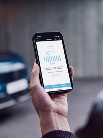 Een vrouw kijkt op haar smartphone bij de PEUGEOT E-3008 Dual Motor